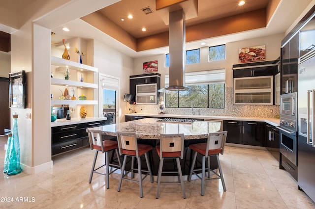 kitchen featuring appliances with stainless steel finishes, light stone countertops, a tray ceiling, a kitchen island, and a breakfast bar