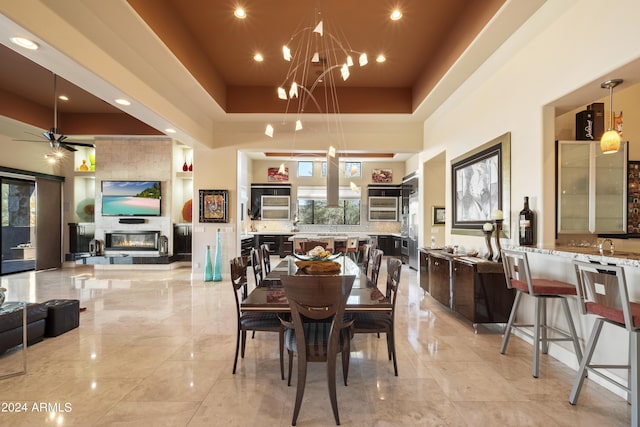 dining area with ceiling fan with notable chandelier, a high ceiling, and a fireplace