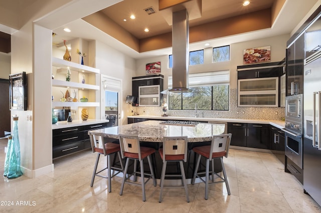 kitchen with stainless steel appliances, a kitchen bar, a tray ceiling, and dark cabinets