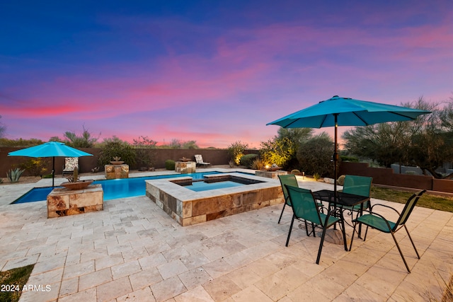 pool at dusk featuring a patio area and an in ground hot tub