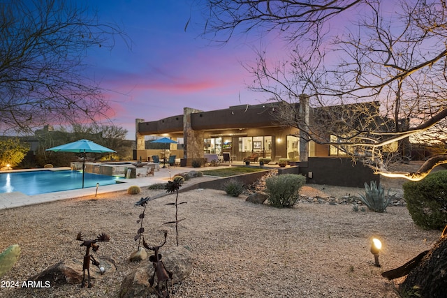 back of house at dusk featuring a patio, fence, a pool with connected hot tub, and stucco siding