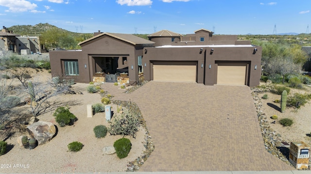 southwest-style home with decorative driveway, a mountain view, an attached garage, and stucco siding