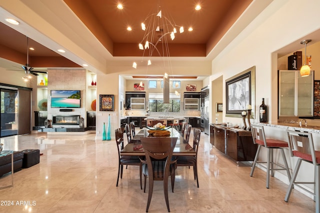 dining area featuring a tray ceiling, ceiling fan with notable chandelier, and a large fireplace