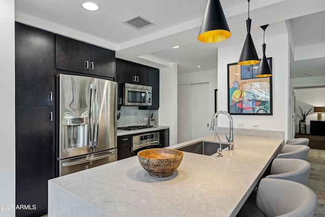 kitchen with stainless steel appliances, visible vents, a sink, dark cabinetry, and a peninsula