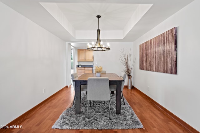 dining space featuring a notable chandelier, wood-type flooring, and a raised ceiling