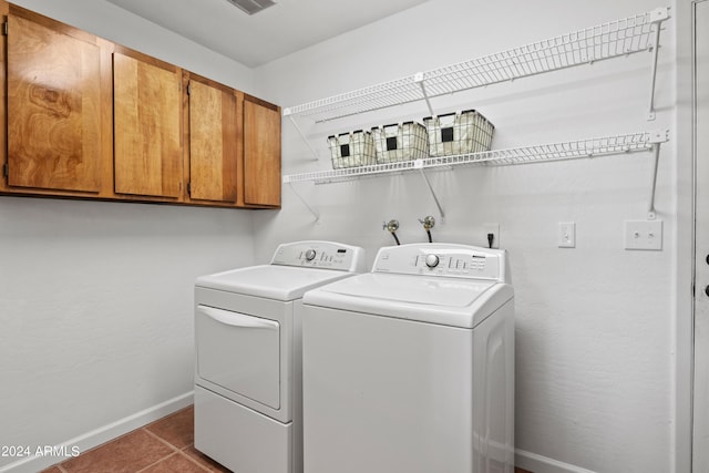 clothes washing area with cabinets, washer and dryer, and dark tile patterned floors