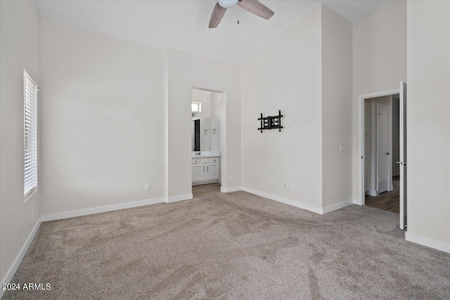 unfurnished bedroom with carpet, ceiling fan, connected bathroom, and a towering ceiling