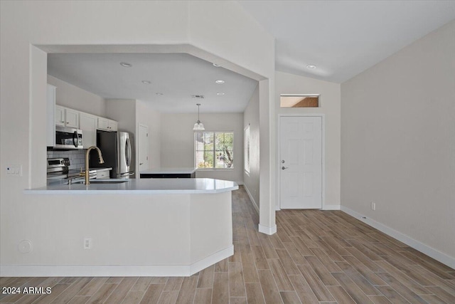 kitchen featuring white cabinetry, tasteful backsplash, light hardwood / wood-style floors, appliances with stainless steel finishes, and lofted ceiling