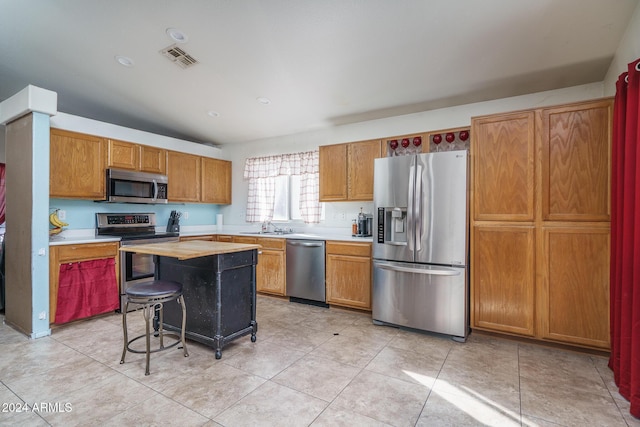 kitchen with sink, stainless steel appliances, light tile patterned floors, a kitchen breakfast bar, and a kitchen island