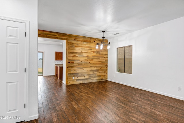 unfurnished dining area featuring dark wood-type flooring, wooden walls, and an inviting chandelier