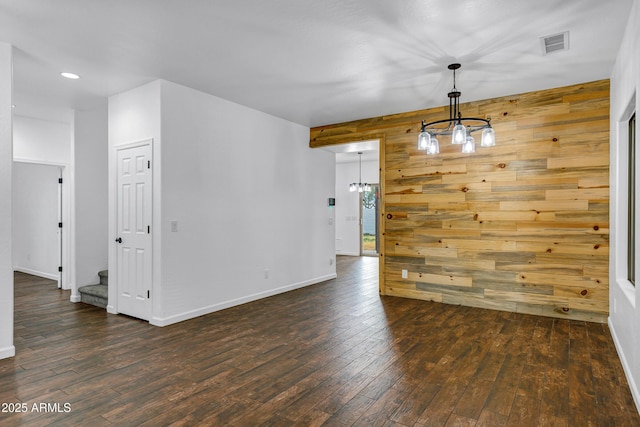 unfurnished dining area featuring dark wood-type flooring, a notable chandelier, and wooden walls