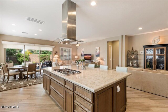 kitchen with stainless steel gas stovetop, island range hood, light wood-type flooring, and a kitchen island