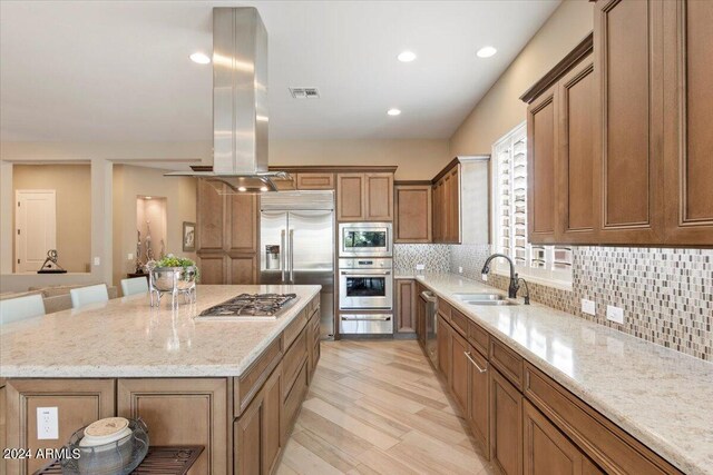 kitchen with a breakfast bar area, built in appliances, light wood-type flooring, a large island, and sink