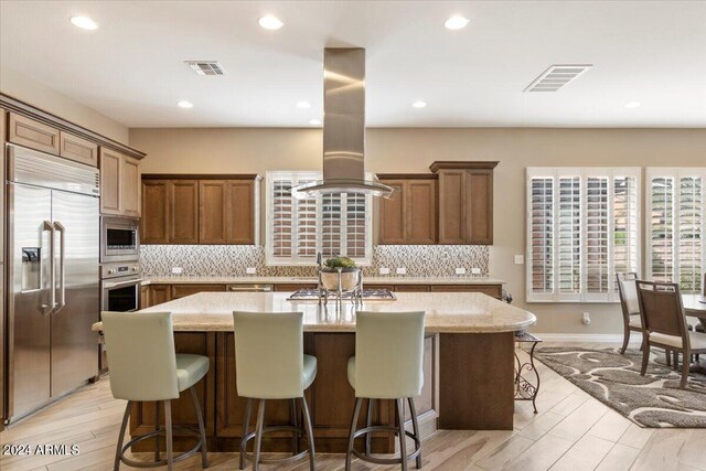 kitchen with light wood-type flooring, island exhaust hood, a center island, and built in appliances