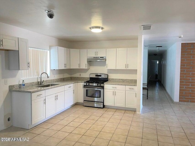 kitchen with light stone countertops, gas range, sink, white cabinetry, and light tile patterned flooring