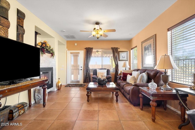 tiled living room with ceiling fan, plenty of natural light, and a fireplace