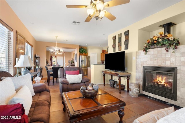 tiled living room with ceiling fan with notable chandelier and a fireplace