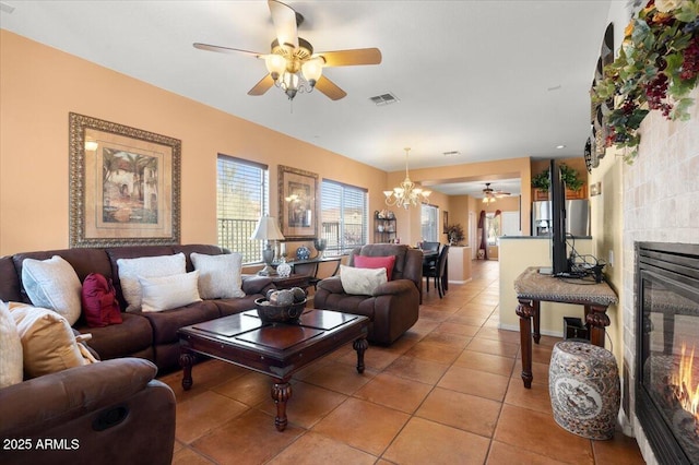 living room featuring light tile patterned floors, ceiling fan with notable chandelier, and a tiled fireplace