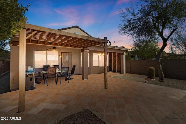 patio terrace at dusk featuring ceiling fan and a pergola