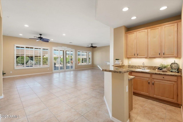 kitchen with sink, light tile patterned floors, light stone counters, and ceiling fan