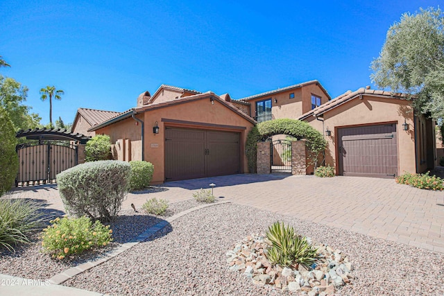 mediterranean / spanish house with a tile roof, stucco siding, an attached garage, decorative driveway, and a gate