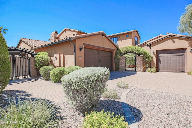 mediterranean / spanish home featuring a tile roof, stucco siding, an attached garage, decorative driveway, and a gate
