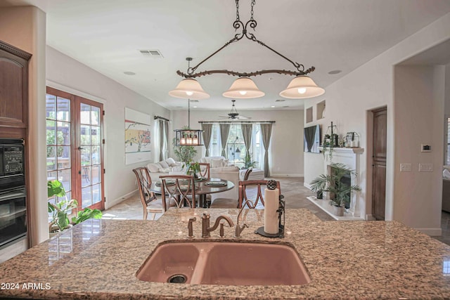 kitchen featuring visible vents, light stone counters, a sink, open floor plan, and a wealth of natural light