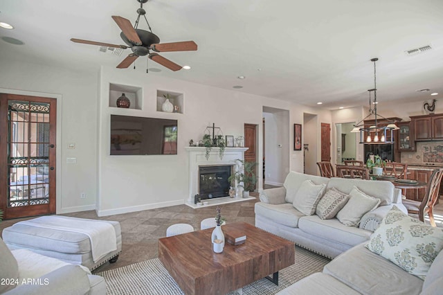 living room with baseboards, visible vents, a glass covered fireplace, and ceiling fan with notable chandelier