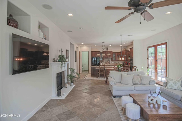 living room featuring baseboards, recessed lighting, a ceiling fan, a glass covered fireplace, and stone tile floors