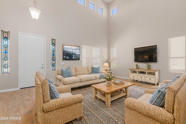 living room with light wood-type flooring, a towering ceiling, and a wealth of natural light