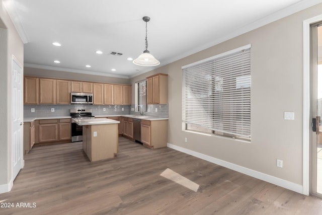 kitchen featuring sink, hanging light fixtures, ornamental molding, a kitchen island, and stainless steel appliances