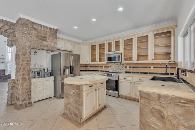 kitchen with stainless steel appliances, a sink, a kitchen island, light countertops, and glass insert cabinets