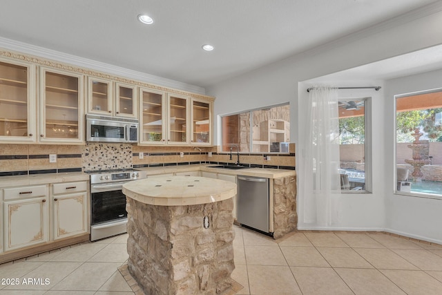 kitchen with stainless steel appliances, tasteful backsplash, light countertops, glass insert cabinets, and a kitchen island