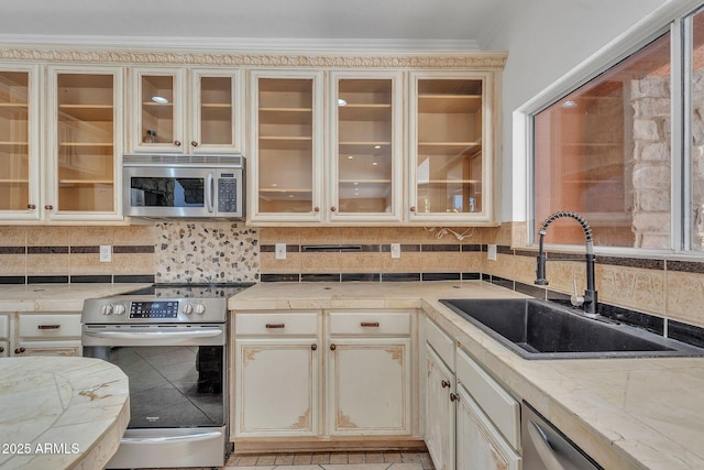 kitchen featuring appliances with stainless steel finishes, light countertops, glass insert cabinets, and a sink