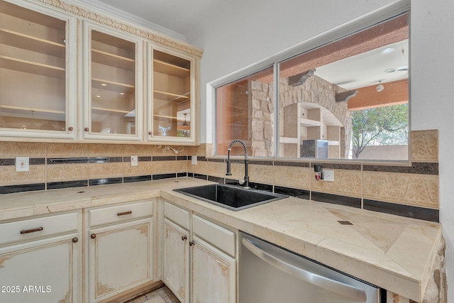 kitchen featuring a sink, light countertops, cream cabinetry, dishwasher, and glass insert cabinets