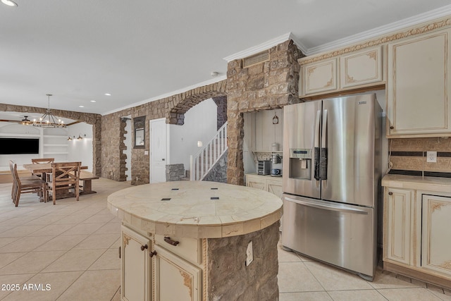 kitchen featuring a center island, crown molding, light tile patterned floors, cream cabinets, and stainless steel fridge