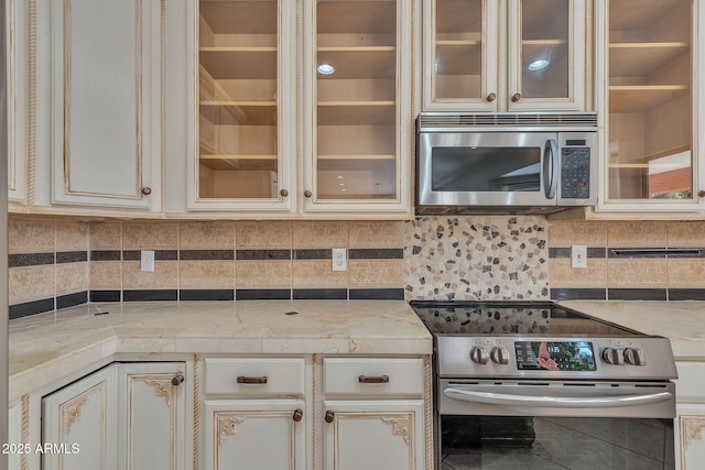 kitchen featuring tasteful backsplash, glass insert cabinets, stainless steel appliances, and light stone counters