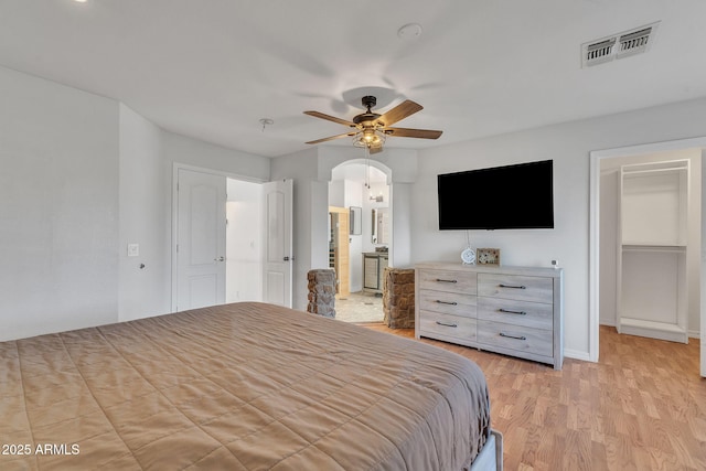 bedroom featuring arched walkways, light wood finished floors, visible vents, a ceiling fan, and baseboards