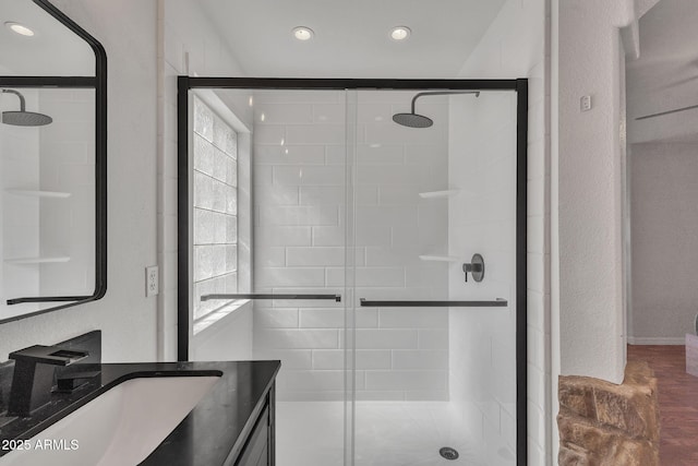 full bathroom with a textured wall, a shower stall, and vanity