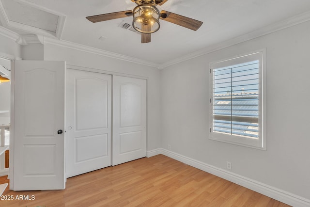 unfurnished bedroom featuring attic access, baseboards, ornamental molding, light wood-type flooring, and a closet