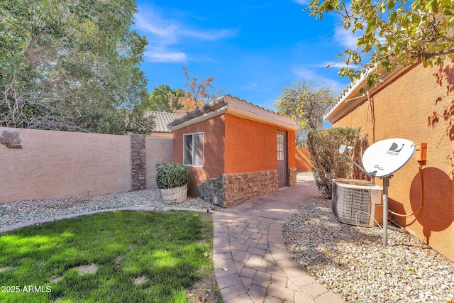 view of side of property featuring a fenced backyard, central AC, a tile roof, stone siding, and stucco siding