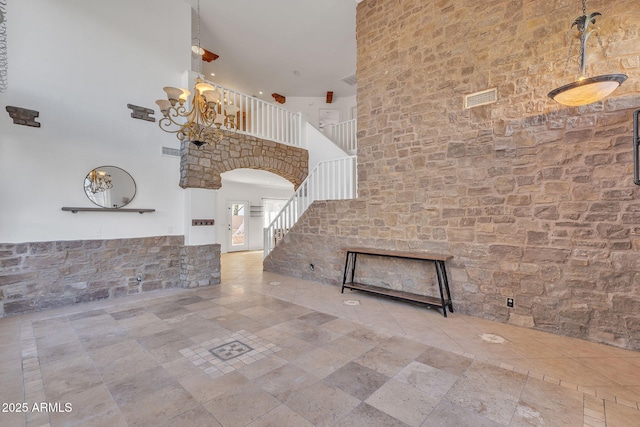 entrance foyer featuring arched walkways, visible vents, stairway, a towering ceiling, and stone finish flooring