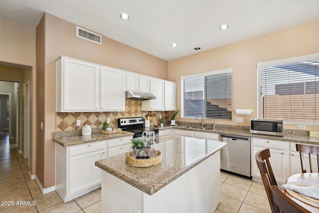 kitchen with light stone countertops, stainless steel appliances, a kitchen island, and sink