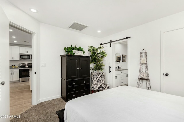 bedroom with a barn door, ensuite bathroom, and light hardwood / wood-style floors