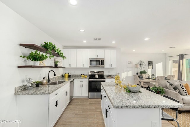 kitchen with sink, light stone countertops, light hardwood / wood-style floors, white cabinetry, and stainless steel appliances