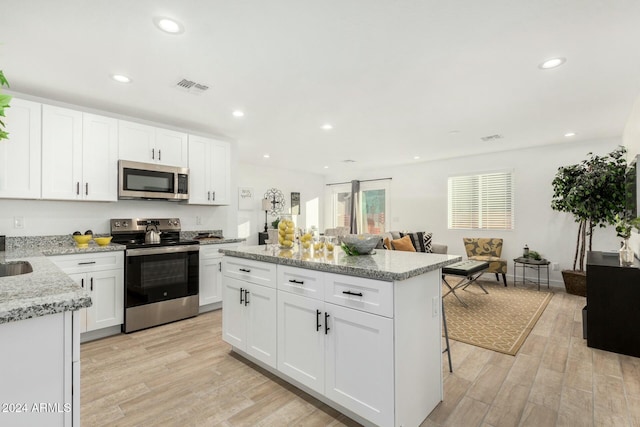 kitchen featuring light stone countertops, appliances with stainless steel finishes, a kitchen breakfast bar, light hardwood / wood-style floors, and white cabinetry