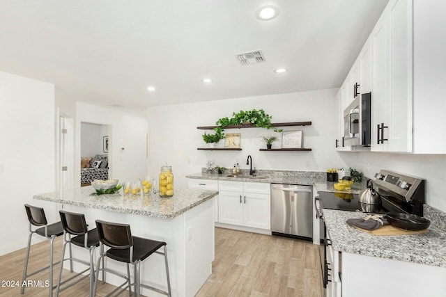 kitchen featuring sink, stainless steel appliances, a kitchen island, white cabinets, and light wood-type flooring