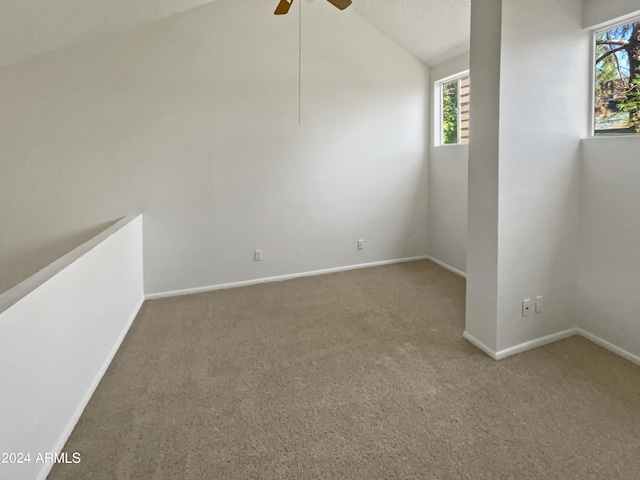 carpeted spare room featuring a textured ceiling, vaulted ceiling, and ceiling fan