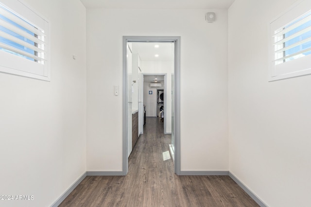 hallway with stacked washer and clothes dryer and dark hardwood / wood-style floors