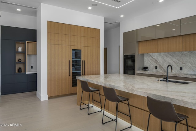 kitchen featuring a breakfast bar, sink, double oven, light stone countertops, and light hardwood / wood-style floors